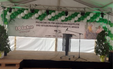 Das Bild zeigt einen Ausschnitt der Bühne mit grün-weißen-Luftballons und einem Banner, das auf das 10-jährige Jubiläum hinweist.