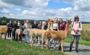 Die Schülerinnen stehen zusammen mit ihrer Lehrerin und den Alpakas, die sie zur Wanderung führen, zu einem Gruppenfoto zusammen.