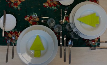 Das Bild zeigt einen weihnachtlich geschmückten Tisch. Auf den Tellern sind Servietten in Form von Tannenbäumen bereitgelegt.