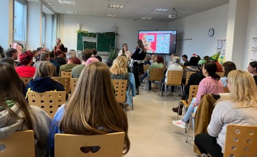 Das Bild zeigt die Schüler:innen und Lehrkräfte, wie sie mit Blick zur Tafel in Reihen hintereinander auf Stühlen sitzen.