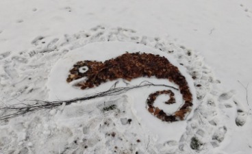 Ein Chamäleon gelegt aus Stöcken und Blättern im Schnee.