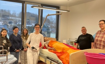 Mehrere Personen stehen an einem Pflegebett, in dem ein Dummy liegt.