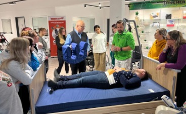 Mehrere Menschen stehen um ein Pflegebett herum. Eine Person liegt auf dem Bett.