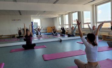 Mehrere Personen sitzen auf Yogamatten in einem hellen Raum und strecken die Arme nach oben